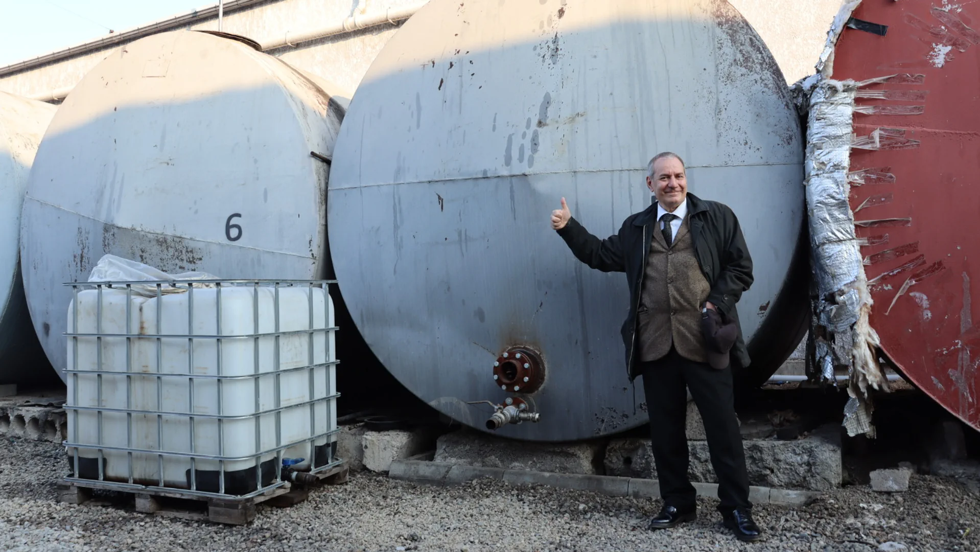 Lachender Mann steht vor einem Tank und macht Daumen-Hoch-Zeichen.