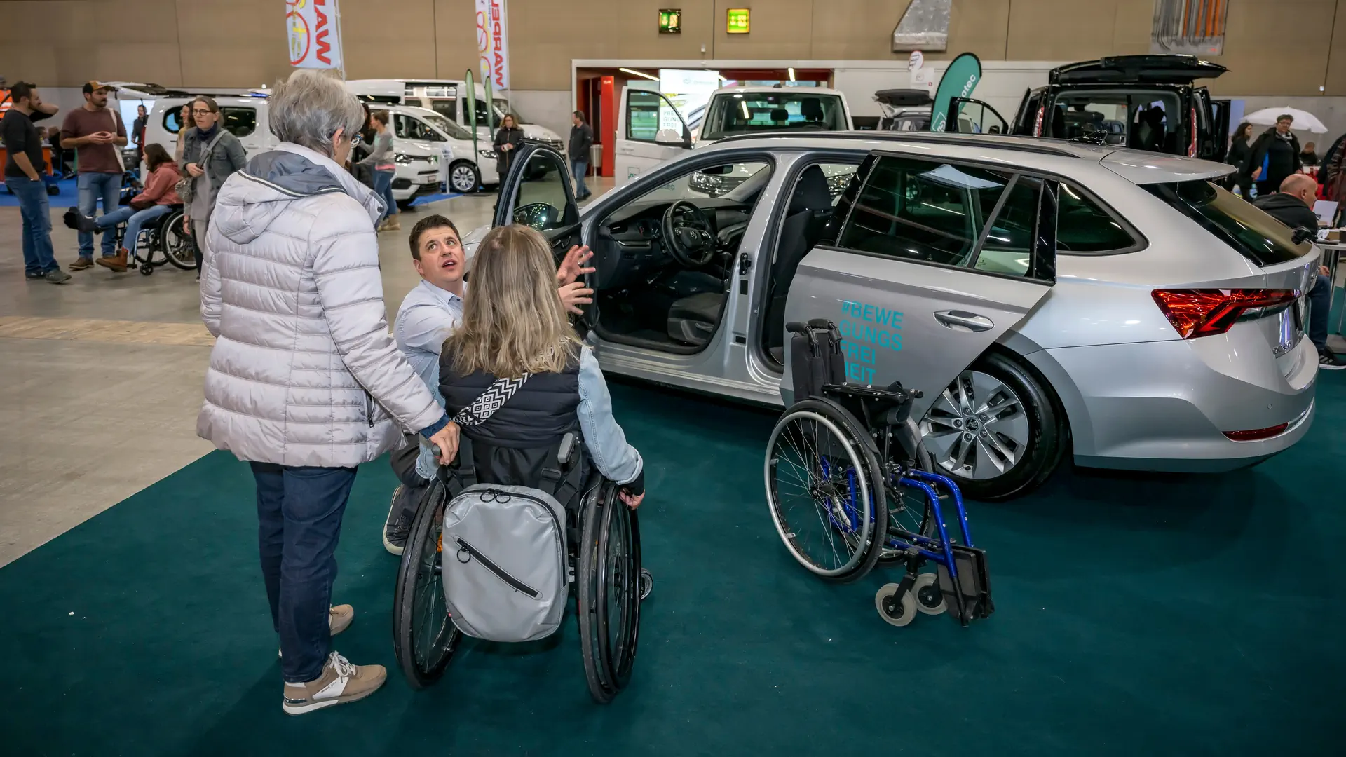 Auf dem Bild sind zwei Rollstuhlfahrer in einer Messehalle zu sehen.