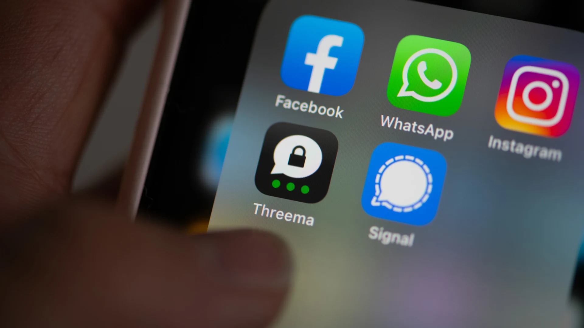 Daumen auf Smartphone-Bildschirm. Darauf sind die Logos verschiedener Social-Media-Apps zu sehen: Facebook, WhatsApp,  Instagram, Threema und Signal.