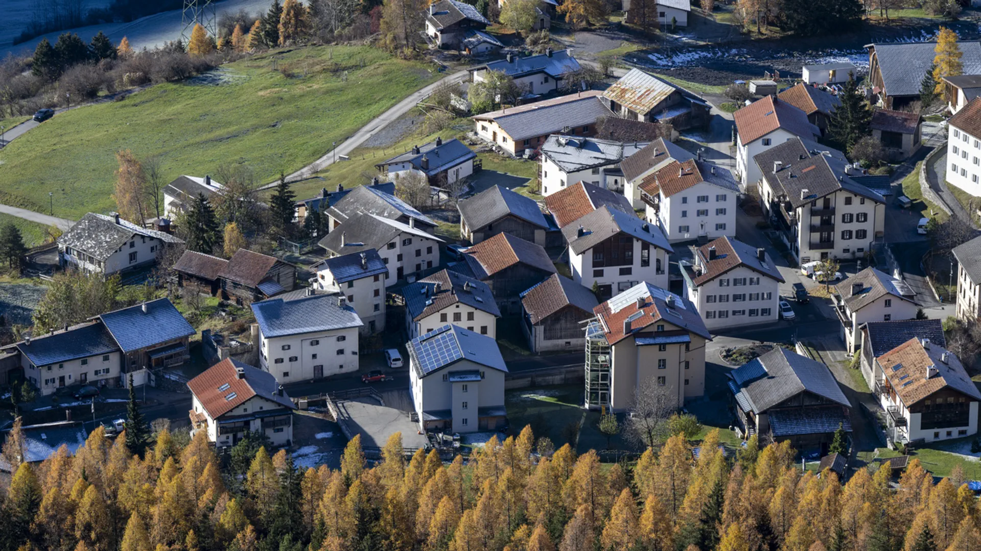 Blick auf das Dorf von oben, im Vorder- und Hintergrund herbstlich gelbe Lärchen.