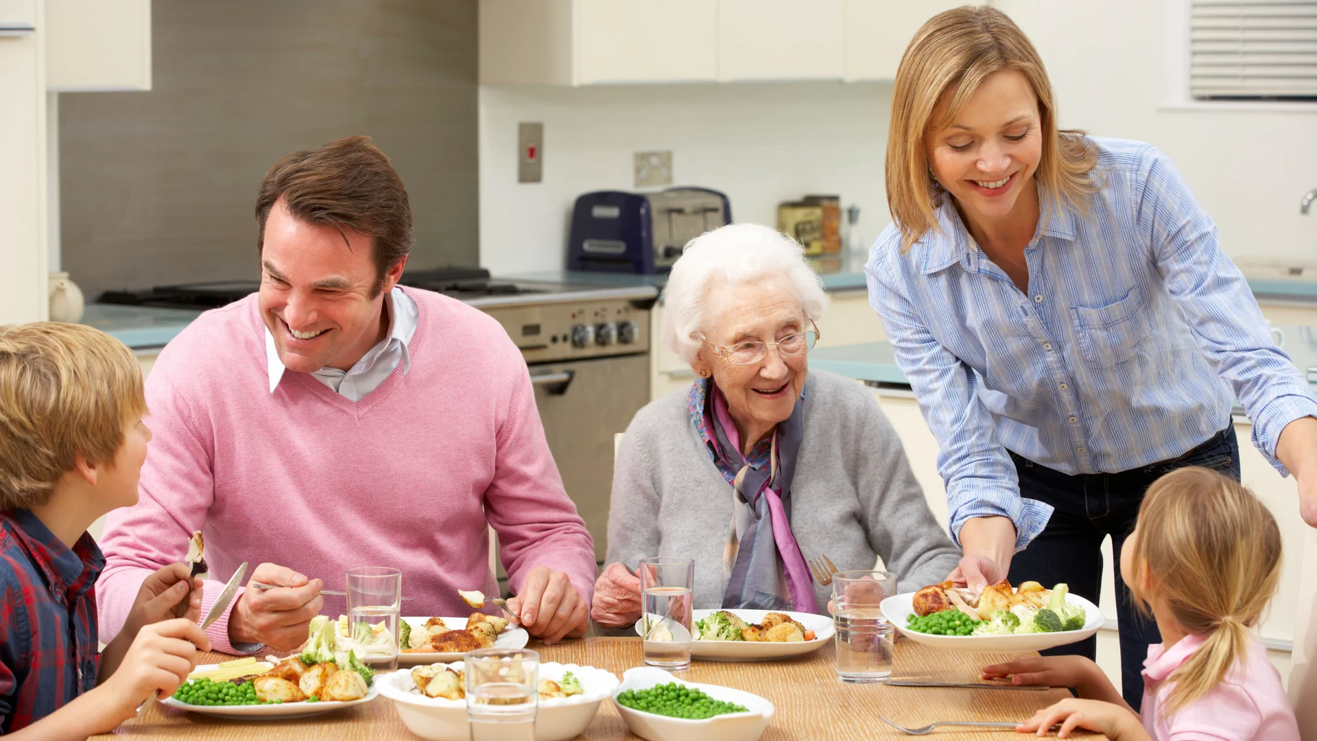 Eine Familie mit Vater, Mutter, Sohn, Tochter und Grossmutter sitzen am Tisch und essen