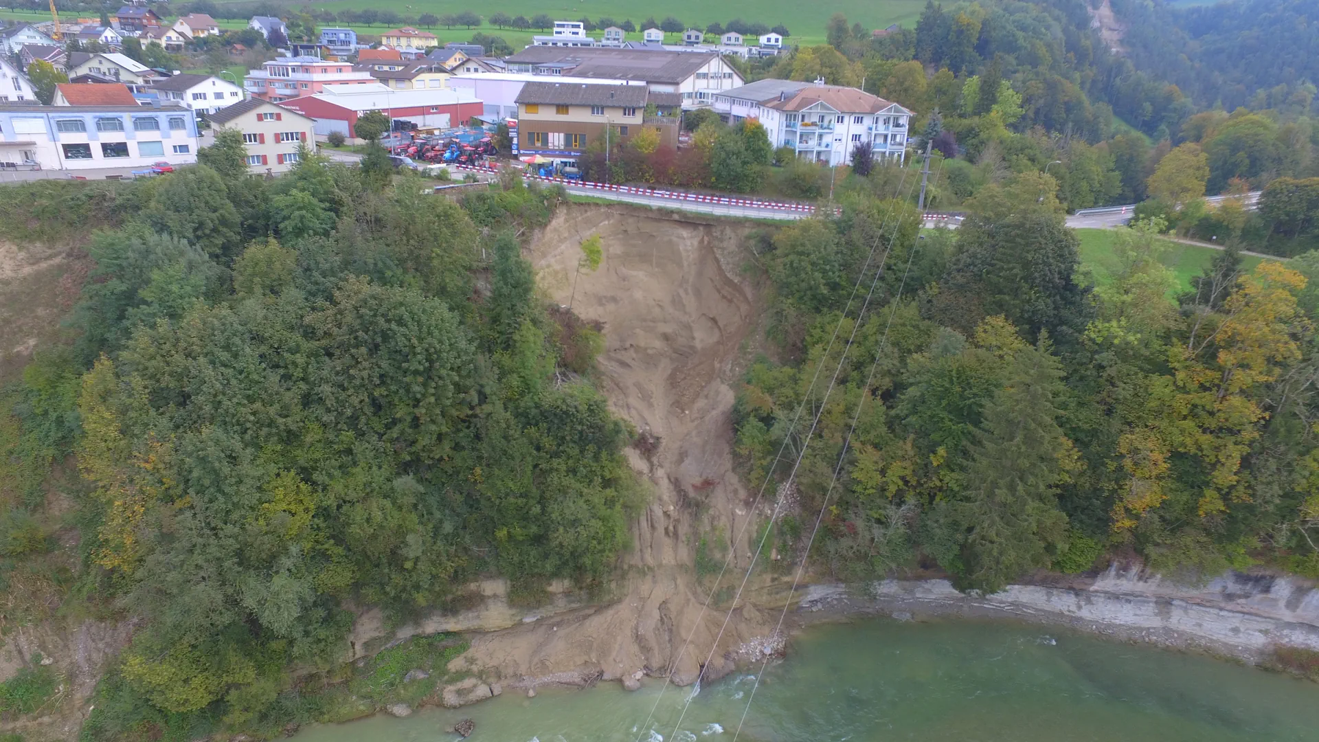 Unterhalb einer Strasse löst sich das Erdreich und rutscht in einen Fluss.