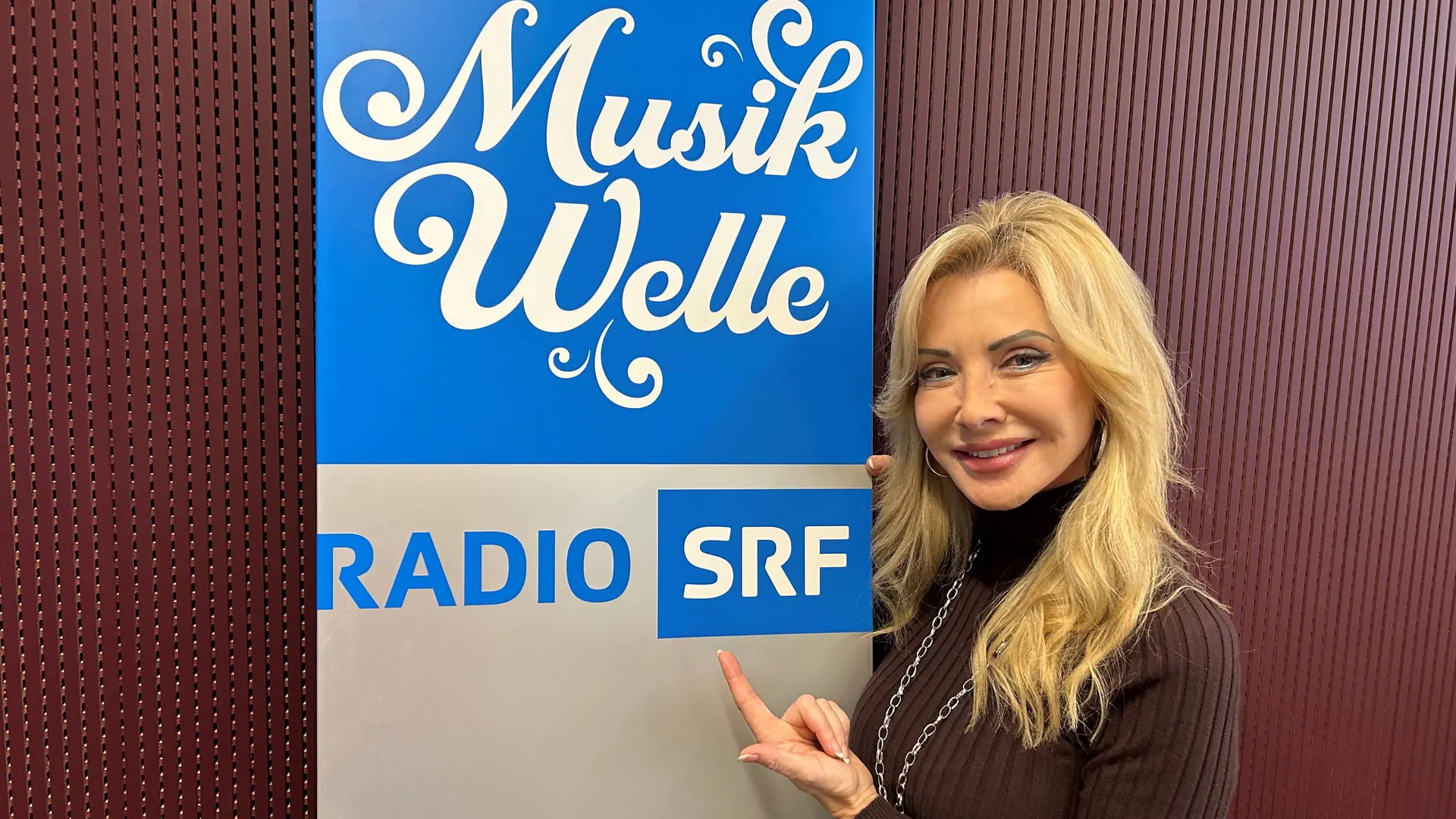 Sängerin Marianne Cathomen steht vor dem Logo der SRF Musikelle