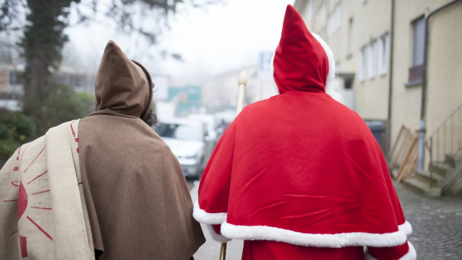 Ein Schmutzli und ein Samichlaus laufen auf der Strasse in Richtung eines Hauses.