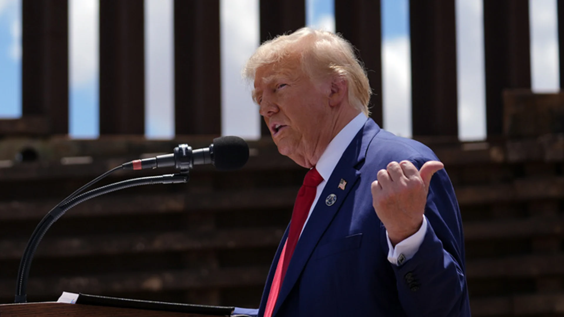 Das Bild zeigt den designierten US-Präsidenten bei einem Besuch an der US-Südgrenze zu Mexiko im August. Trump spricht an einem Rednerpult und zeigt mit der Hand nach hinten.