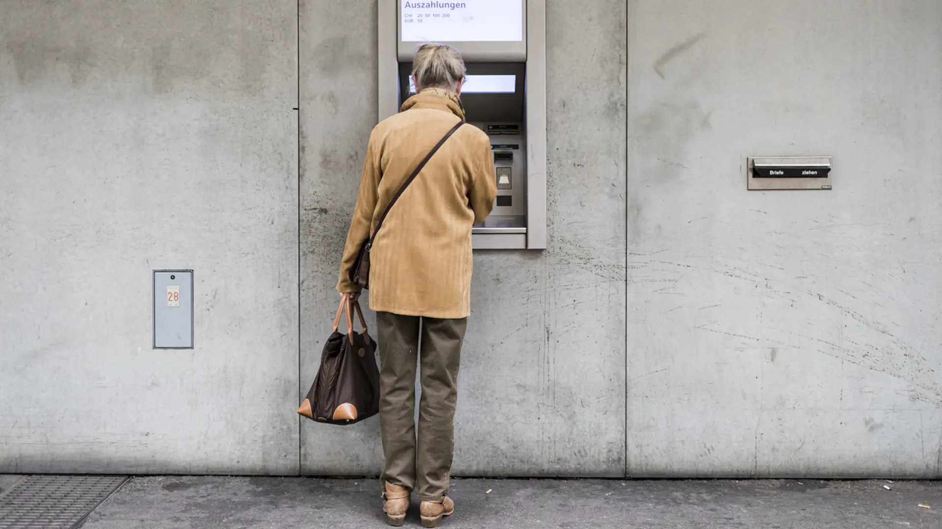 Seniorin steht vor einem Bankomat.