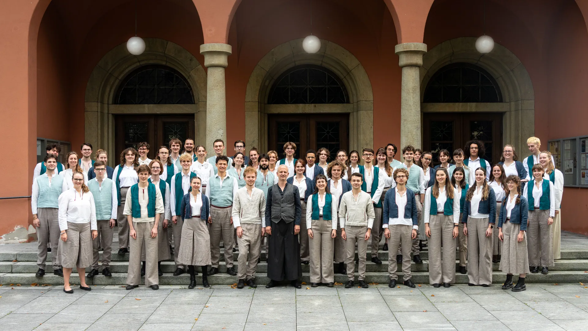 Der Schweizer Jugendchor steht vor einem roten Gebäude mit Säulen.