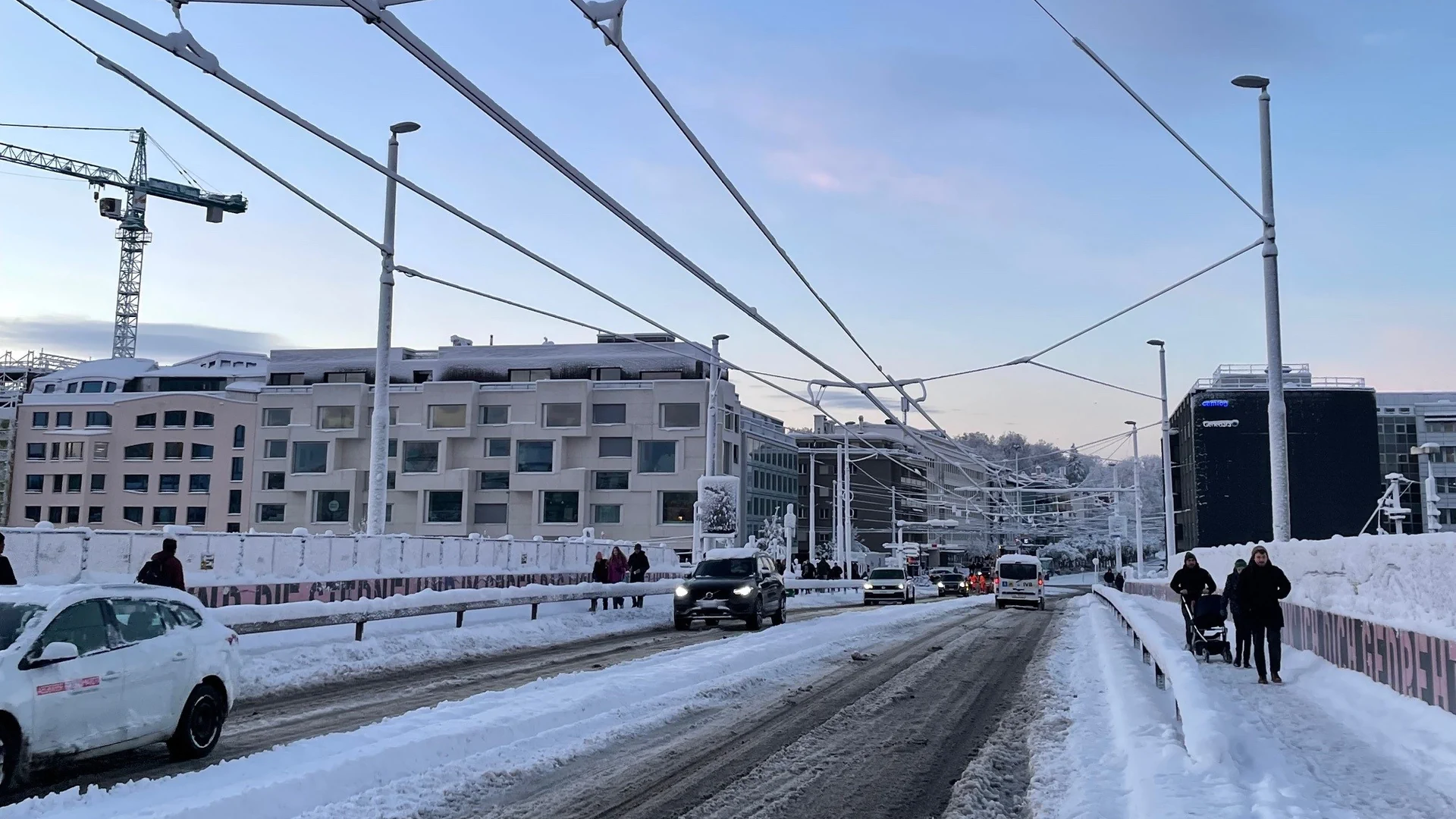 Margarethenbücke mit verschneiten Tramfahrleitungen und Schnee auf Strasse und Trottoirs. Einige Autos und Menschen sind unterwegs.