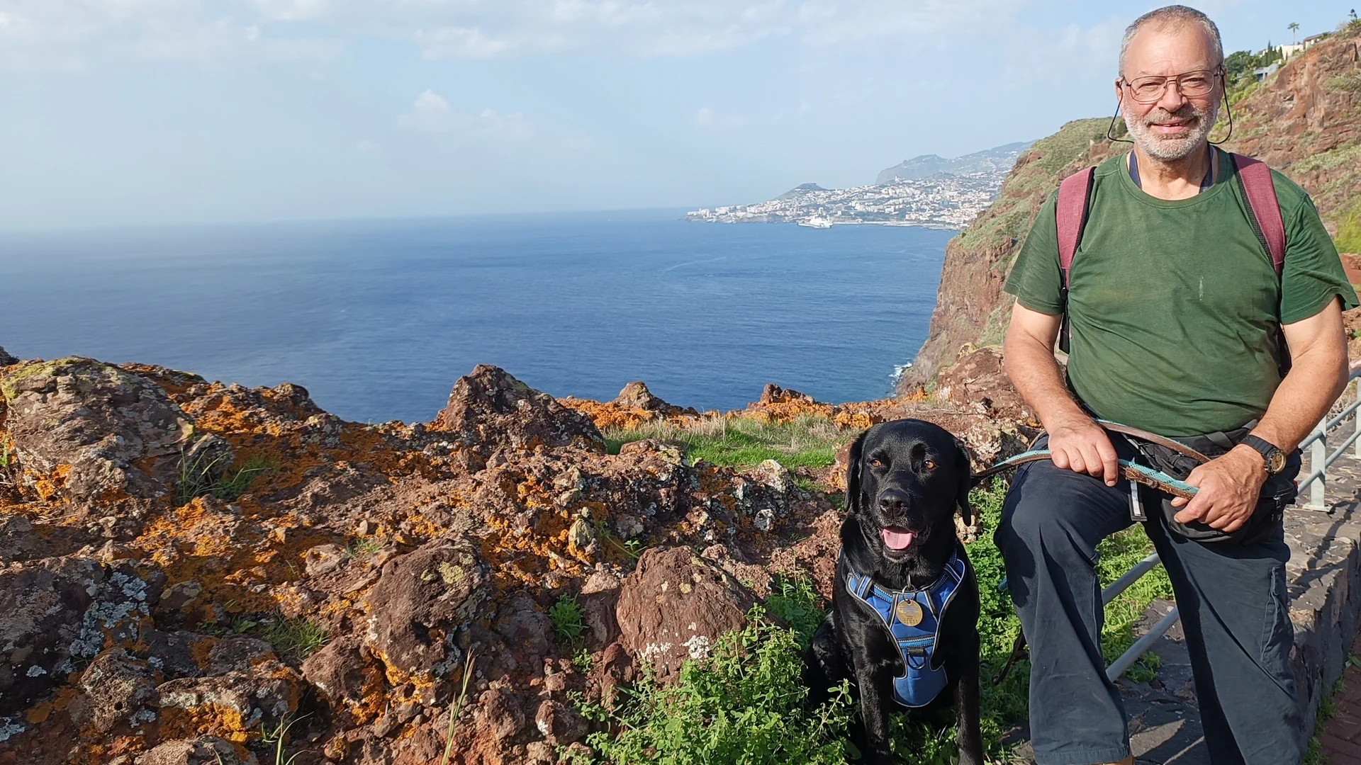 Jürg Peter steht mit Hündin Zampa auf einen Aussichtspunkt. Im Hintergrund sieht man das Meer und die Küste von Madeira.