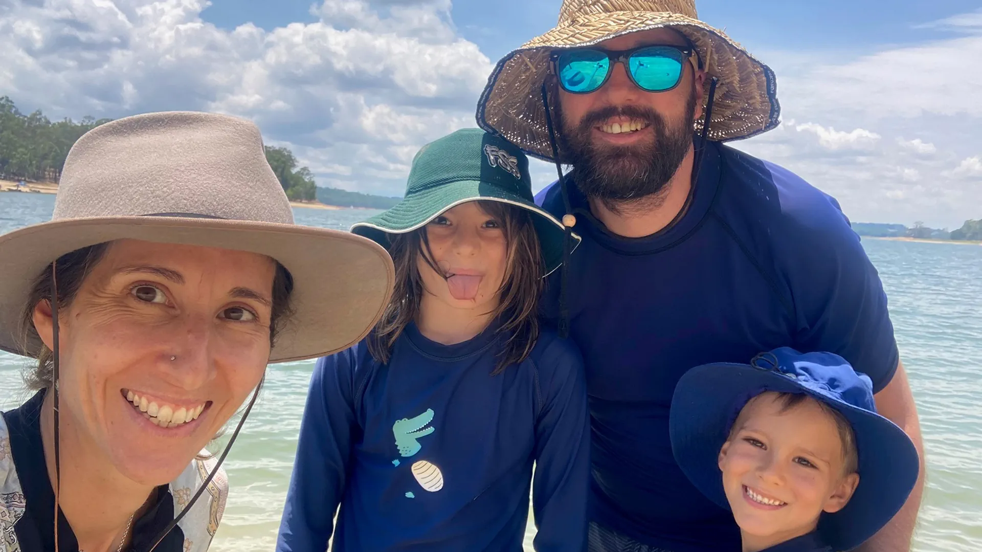 Franziska, Söhne Lenny, Deon und Ehemann Piet posieren am Strand. Alle tragen einen Hut und einen Ganzkörperanzug zum Schwimmen